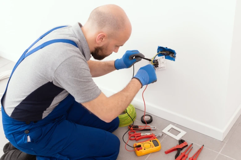 Elektrikář testuje dráty v zásuvce multimetrem během instalace.