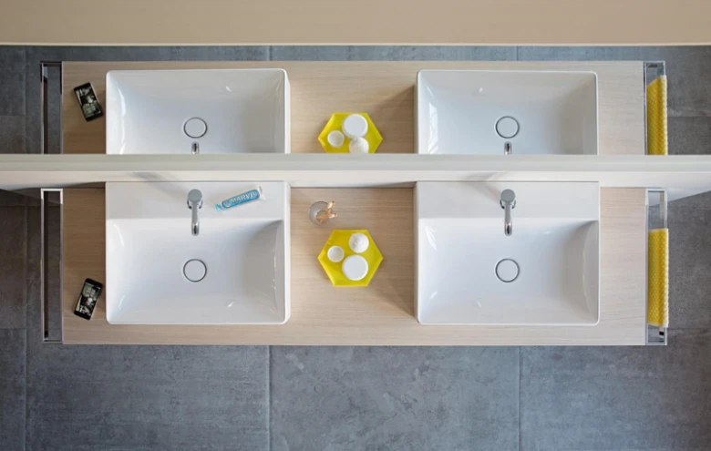Pohled shora na dvě bílá umyvadla v koupelně s moderní instalací.