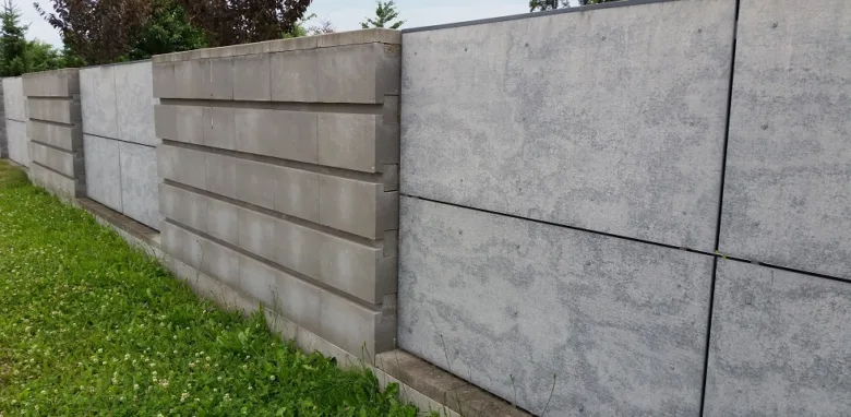 Řada šedých betonových plotů s horizontálními panely vedle trávníku.