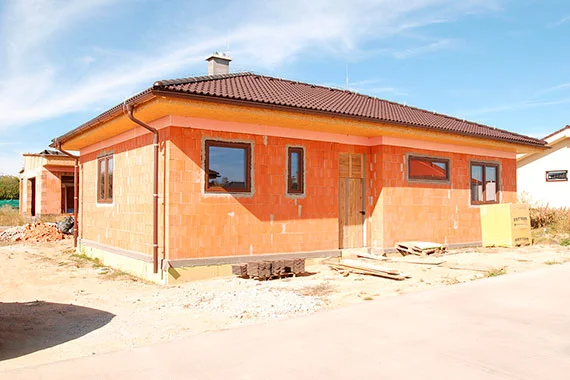 Oranžový dům z porobetonu ve stavbě s okny a střechou.