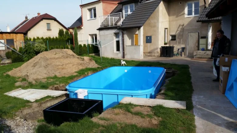 Modrý venkovní bazén se instaluje v zahradě vedle domů.