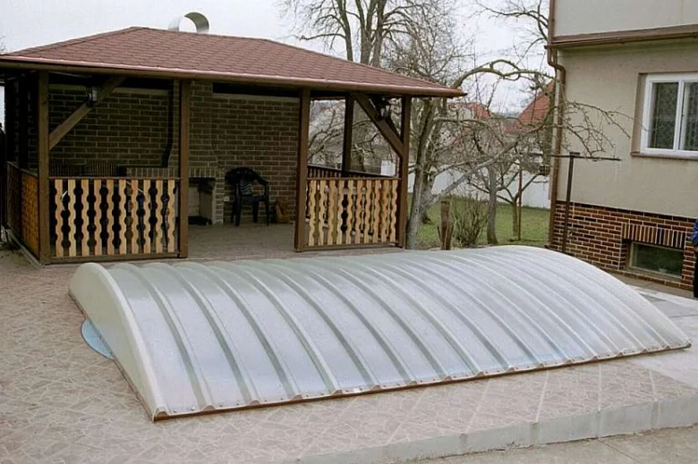 Průhledný kryt bazénu na zahradě vedle altánu.