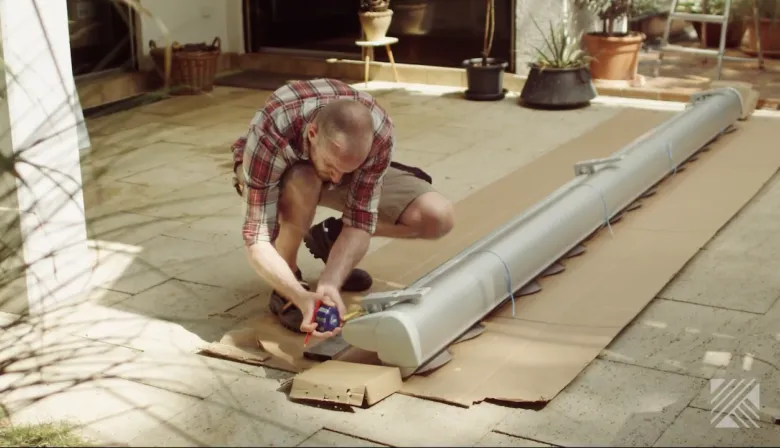 Muž měří část markýzy na balkóně při instalaci.