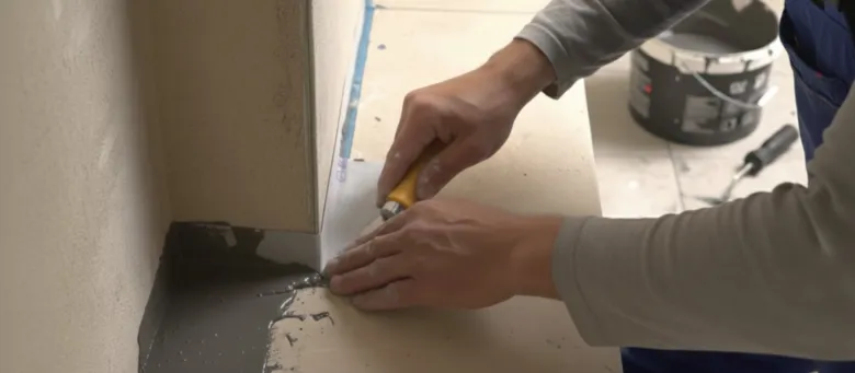 Muž nanáší hydroizolační hmotu do rohu koupelny