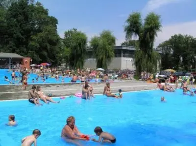Lidé se koupají v bazénu Otrokovice za slunečného dne.