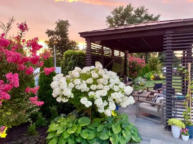 Dřevěná zahradní pergola s posezením uprostřed kvetoucí zahrady.