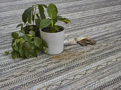Rostliny v hrncích na vzorovaném balkónovém koberci.