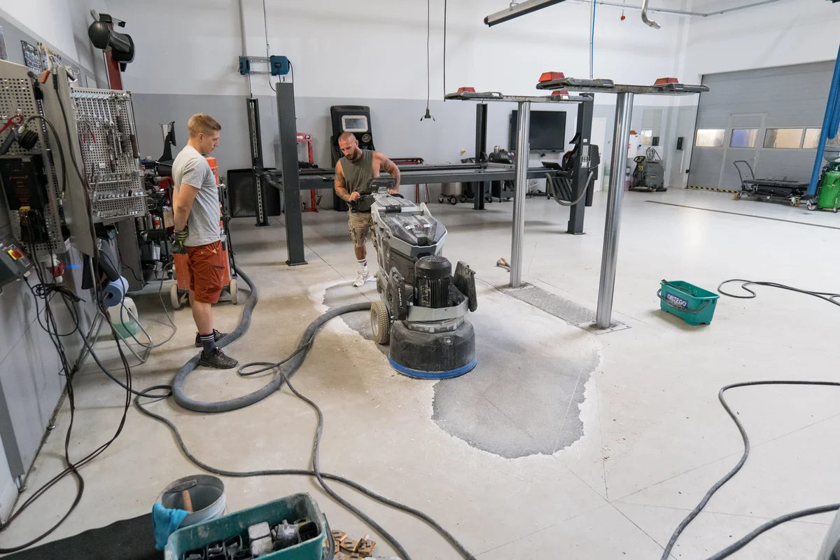 Pracovníci brousí podlahu v garáži s vysavačem pro rychletuhnoucí beton.