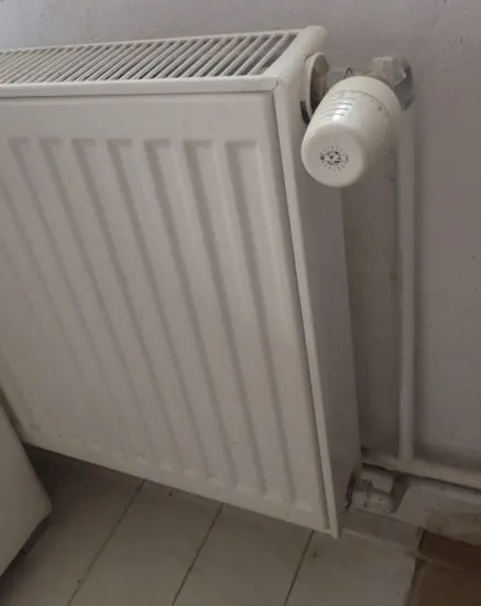 Bílý litinový radiátor s termostatem na zdi.