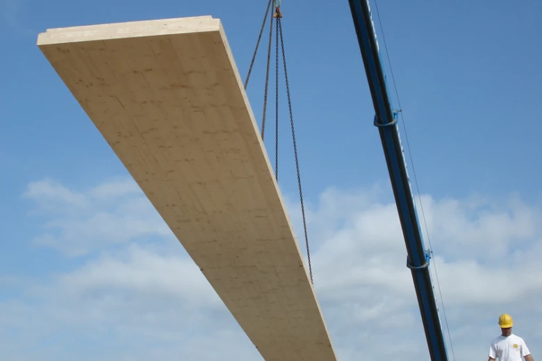 Velký dřevěný CLT panel je zvedán žebřicem na staveništi.