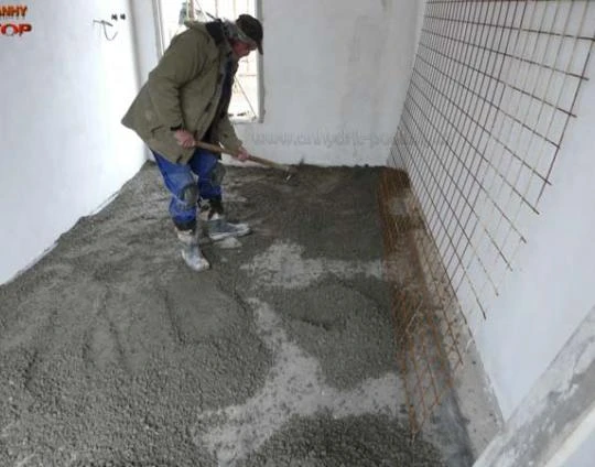 Montáž podlahového topení: pracovník nalévá betonovou vrstvu.