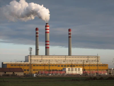 Velká elektrárna na uhlí s třemi vysokými komíny vydávajícími kouř do oblohy.