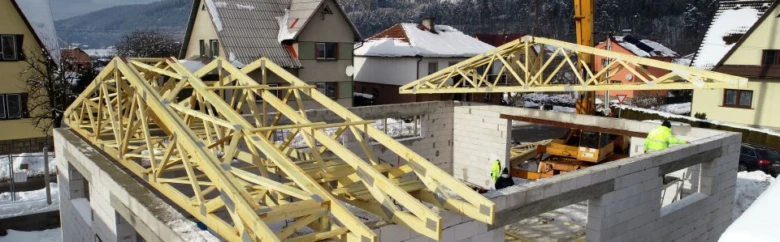Montáž dřevěných vazníků na střeše domu v zimním prostředí.