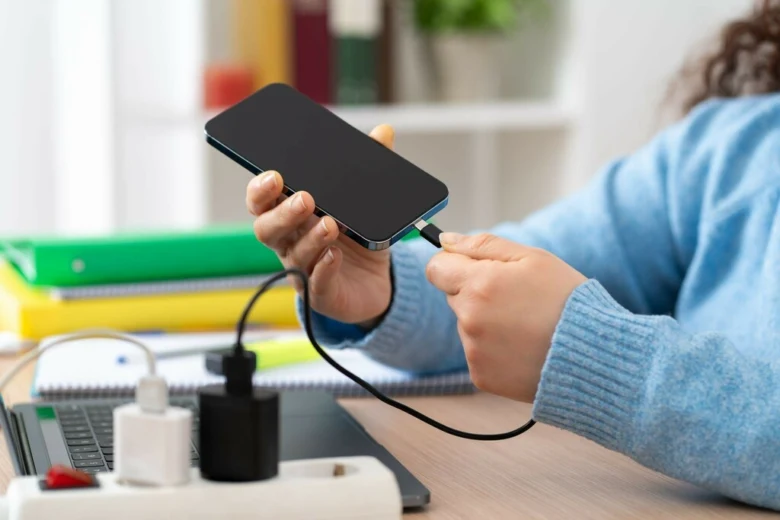 Osoba nabíjí chytrý telefon pomocí kabelu v kancelářském prostředí.