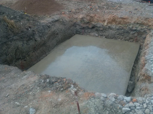 Zalévání betonu pro bazén do vykopaného jámy.
