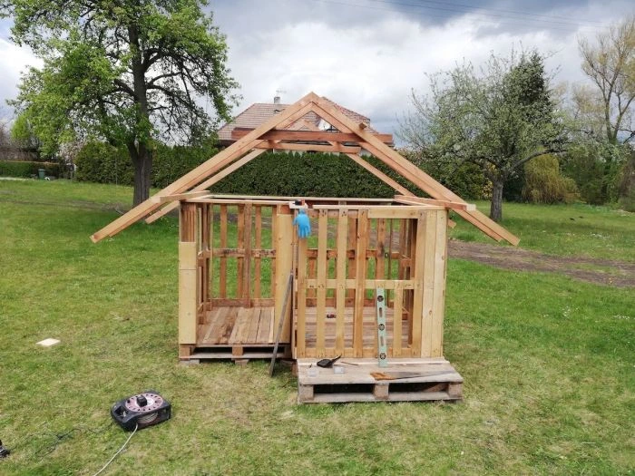 Částečně postavený dřevěný domek z palet na trávníku.