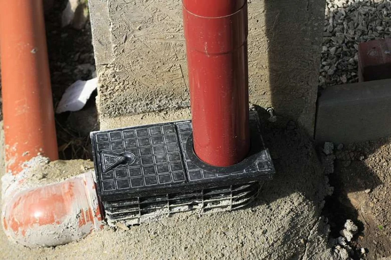 Černý plastový podložník pro okapovou svodnici na betonové zdi.