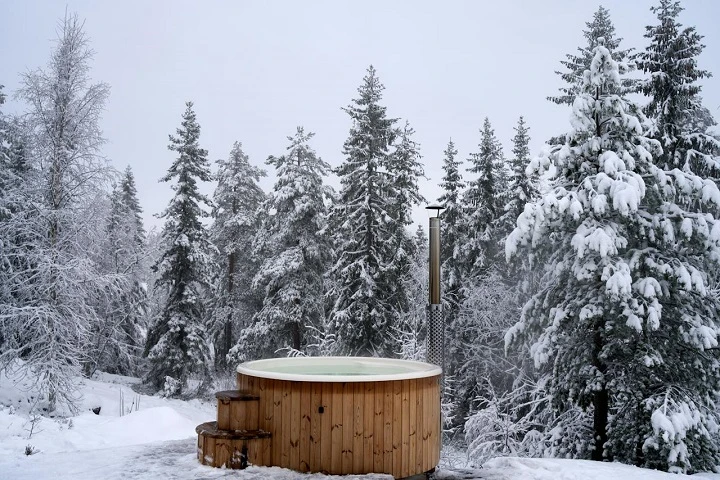 Hot tub z dřeva v zimním lese po svépomocné výrobě.