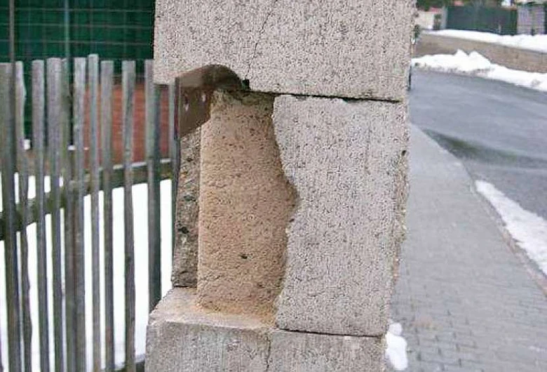 Poškozený betonový plot s odhaleným jádrem upevněným kovovým držákem.