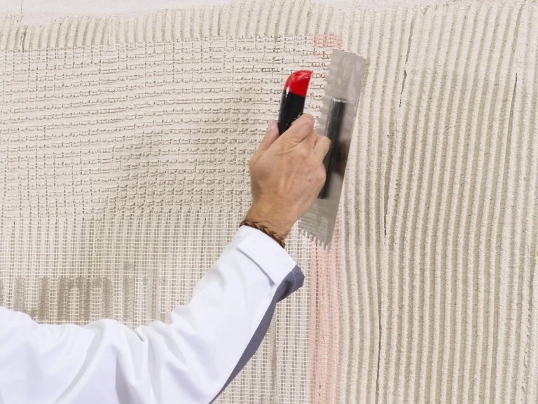 Ruční aplikace materiálu na fasádu s mřížkou pro opravu.