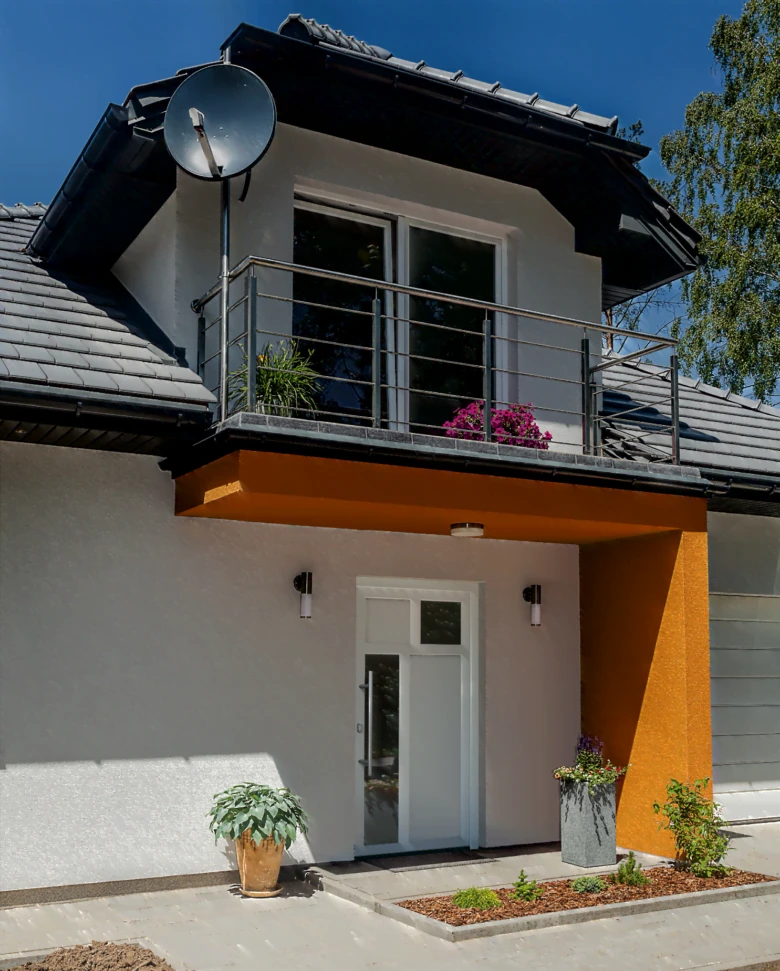 Moderní bílé vstupní dveře do domu s oranžovým přístřeškem.
