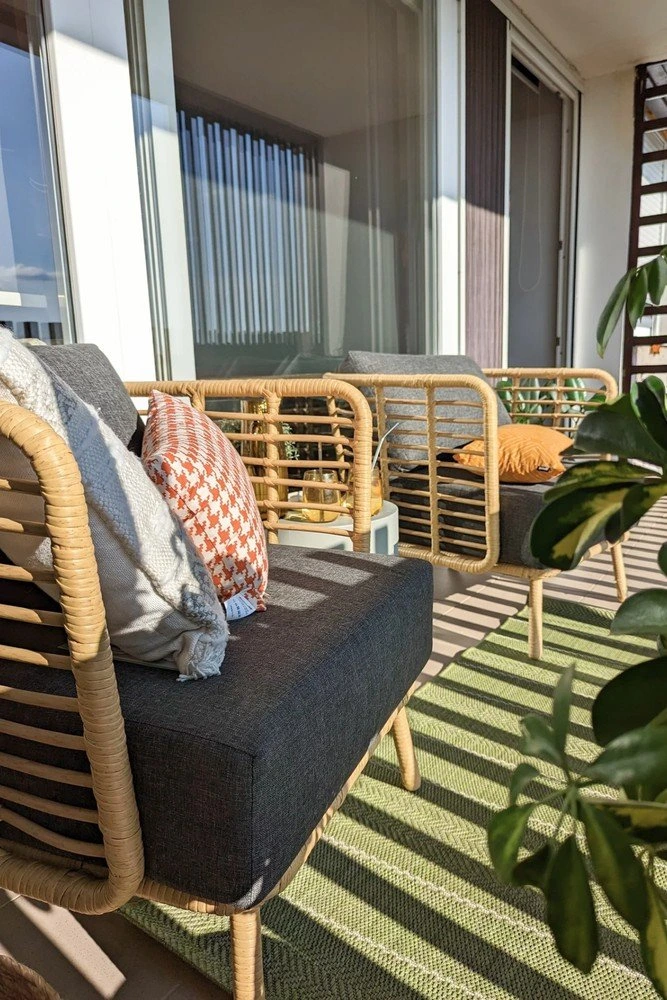Uspořádání malého balkonu s ratanovou židlí a zelenou podlahovou kobercem.