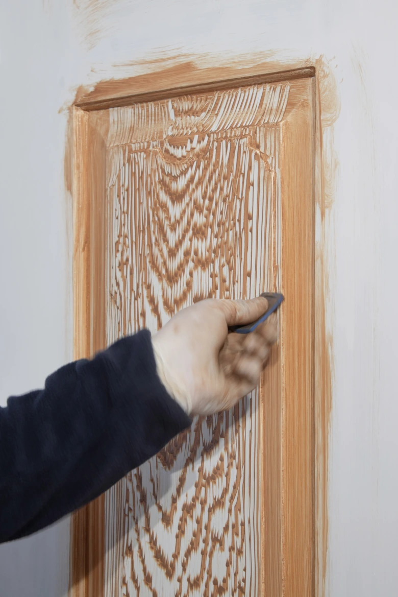 Ruka nanáší dřevoplivu na vyřezaný dřevěný rám dveří.