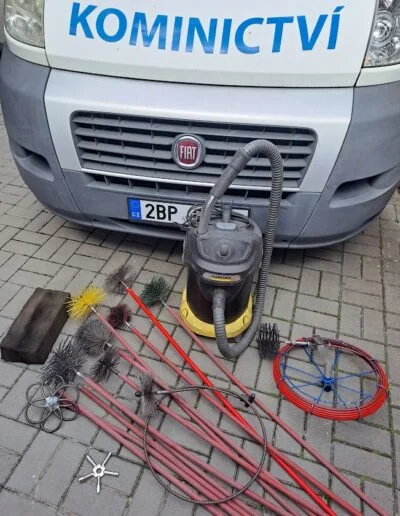 Nástroje pro čištění komínů před služebním vozem s nápisem Kominictví.
