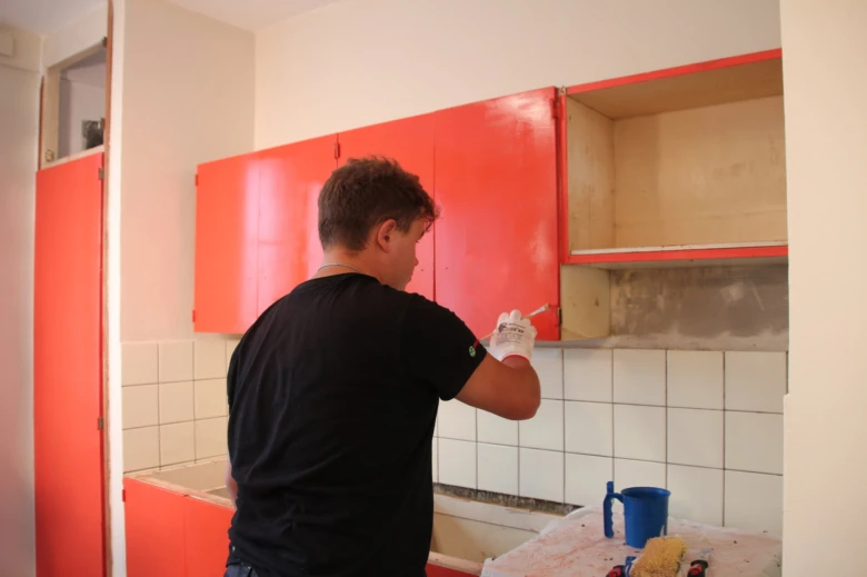 Muž maluje červené kuchyňské skříňky během rekonstrukce.