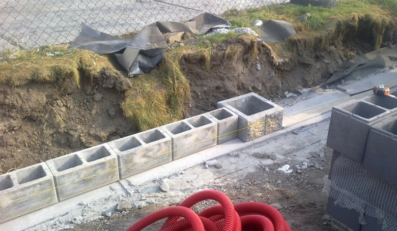 Stavba plotu z betonových tvarnic vedle vykopaného terénu s hydroizolační fólií.