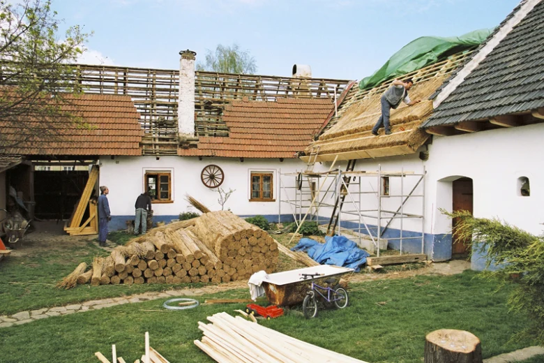 Práce na doškové střechě s dřevem a provizorním lešení.