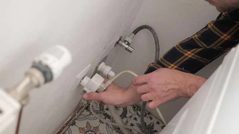 Ruční připojení vodovodních hadic k pračce na stěnu.