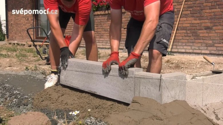 Dva muži pokládají betonový obrubník do čerstvého betonu.