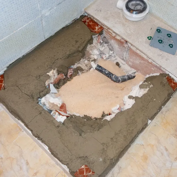 Demontáž sprchového koutu s viditelnými potrubím a zbytky dlažby.