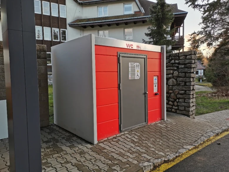 Moderní veřejná toaleta v červené barvě na chodníku.