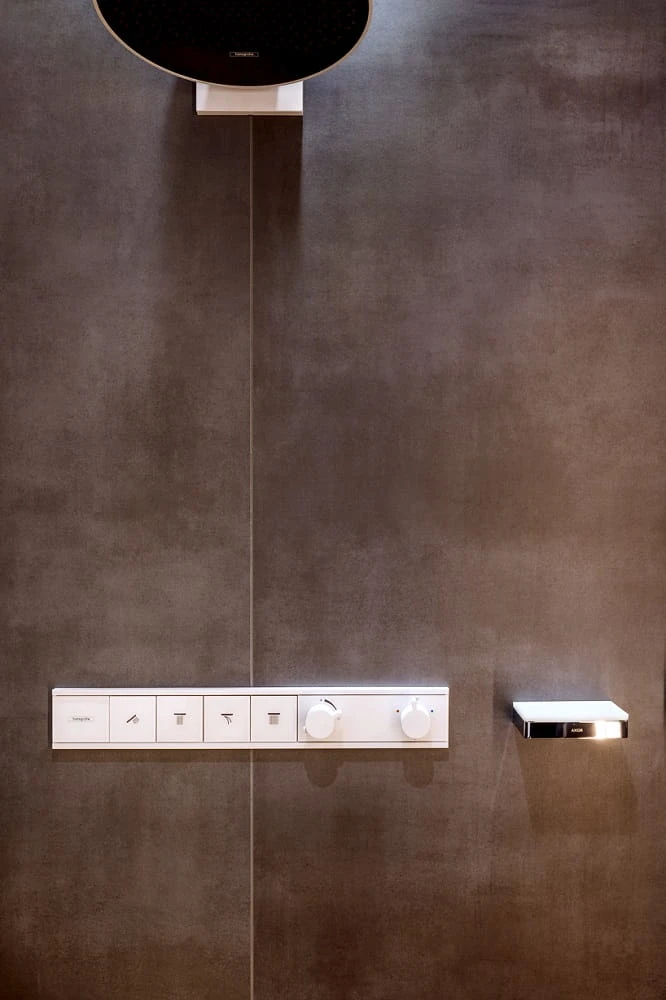Moderní ovládací panel sprchové baterie na tmavé dlažbě.