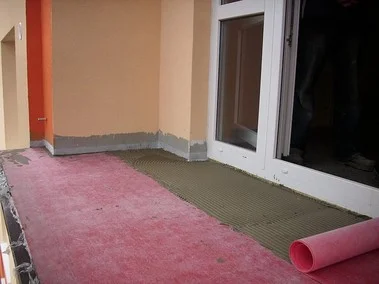 Vrstvy podlahy na balkóně s izolací a lepidlem před dlažbou.
