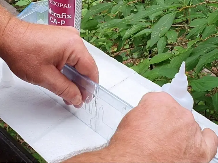 Muž lepi bílý plast pomocí průhledného nástroje a kapátkové lahvičky.