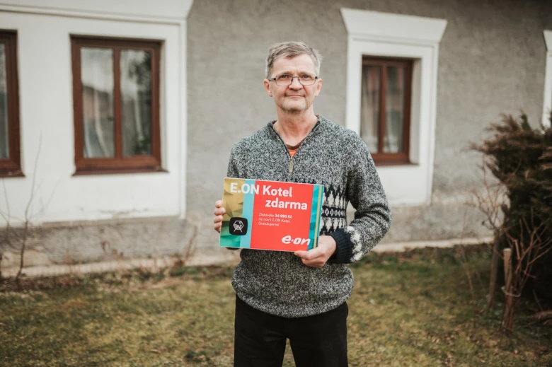 Muž drží krabici plynového kotle před domem.