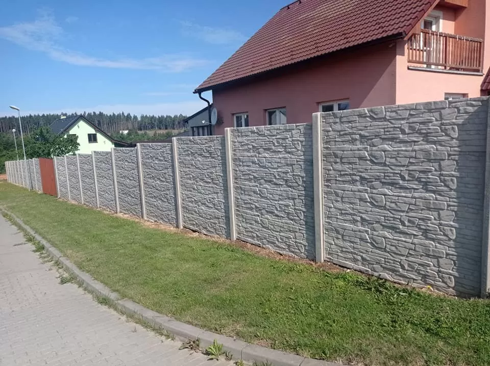 Konkrétní betonový plot s kamennou texturou u domu.