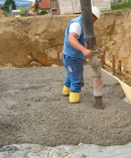 Stavebník nalévá beton z výlevky na základovou plochu.