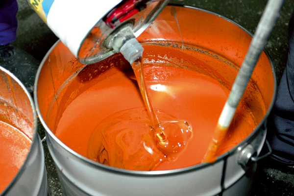 Nalévání oranžové epoxidové stěrky do kbelíku na beton.
