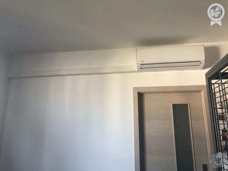 Bílá stěnová jednotka klimatizace nainstalovaná nad dveřmi.