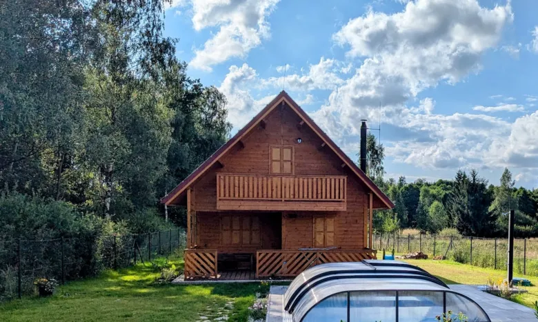 Dvoupatrová dřevěná chata na trávníku obklopená stromy.