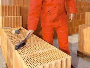 Stavební cihla, kterou kontroluje dělník v oranžovém obleku.