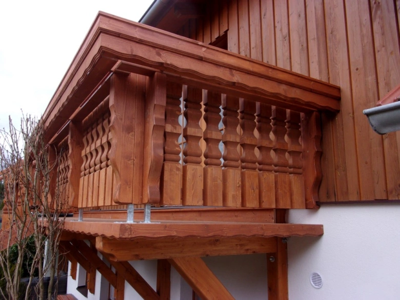 Dřevěný balkon s ozdobnými sloupky připevněný k domu.