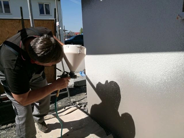 Pracovník stříká fasádu omítkou pomocí spreje.