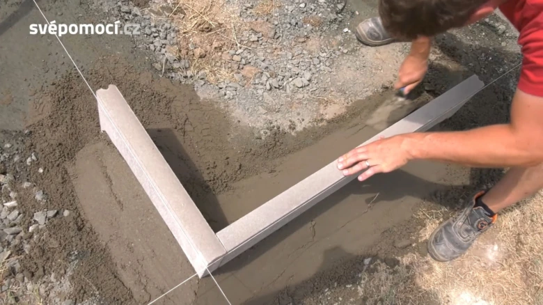 Pracovník vyrovnává beton kolem nově položeného obrubníku.