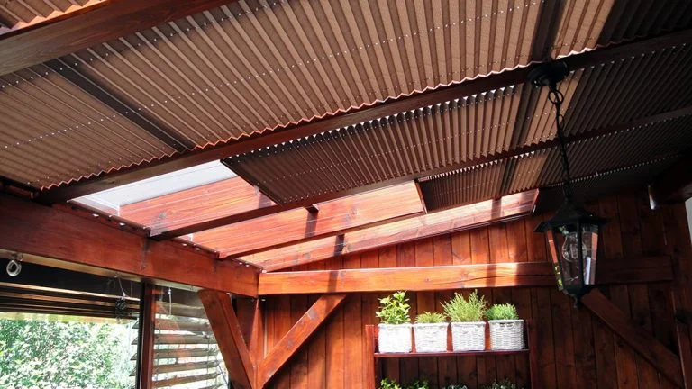 Dřevěná pergola s rostlinami zastíní venkovní prostor u okna.