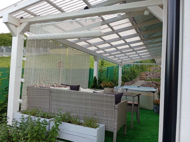 Bílá zahradní pergola s gaučem, stolkem a horkou vanou.